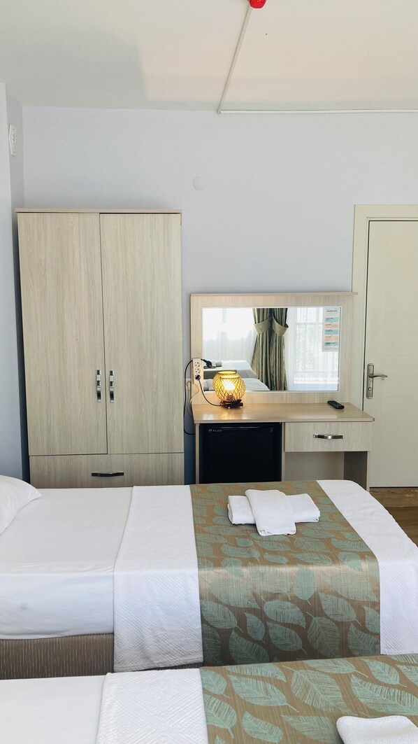 Una habitación de hotel con dos camas, un escritorio con lámpara, un armario y un espejo.
