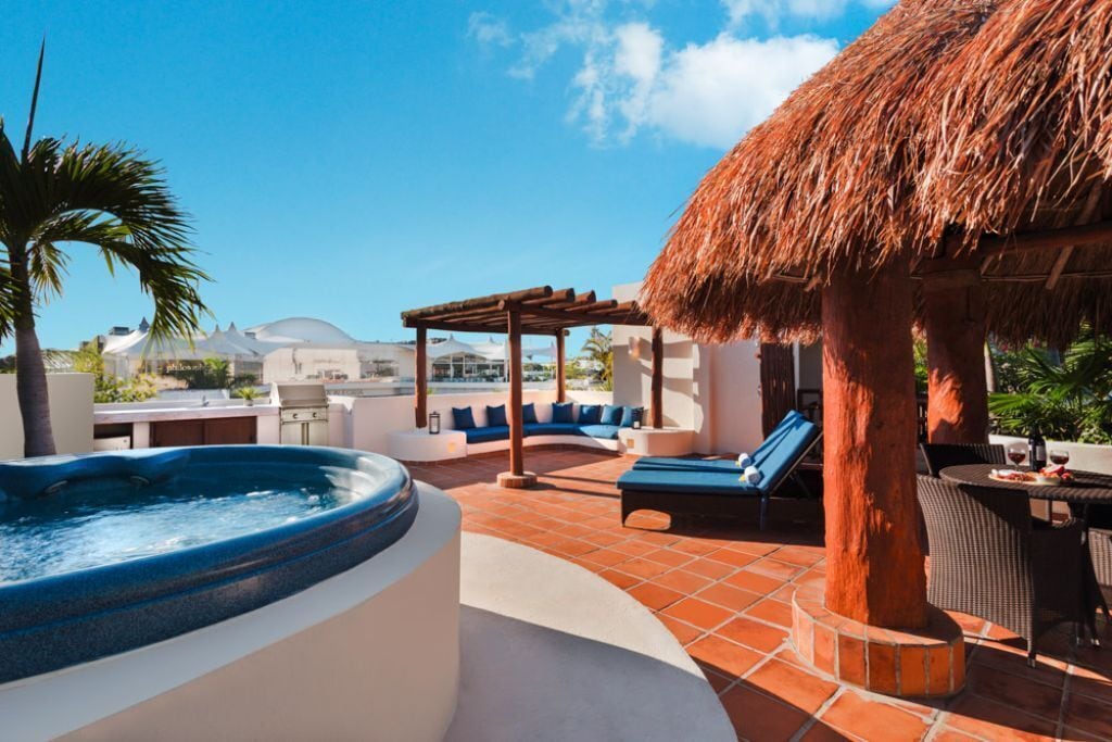 A rooftop pool area with a hot tub, lounge chairs, and a thatched roof structure.