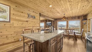 Interior de una cabaña de madera con una isla de cocina, taburetes de bar, paredes de madera y un cuadro enmarcado.