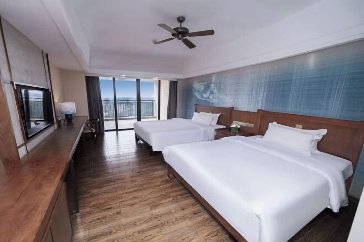 Une chambre d’hôtel avec deux lits, un ventilateur de plafond, une télévision et un balcon avec vue.