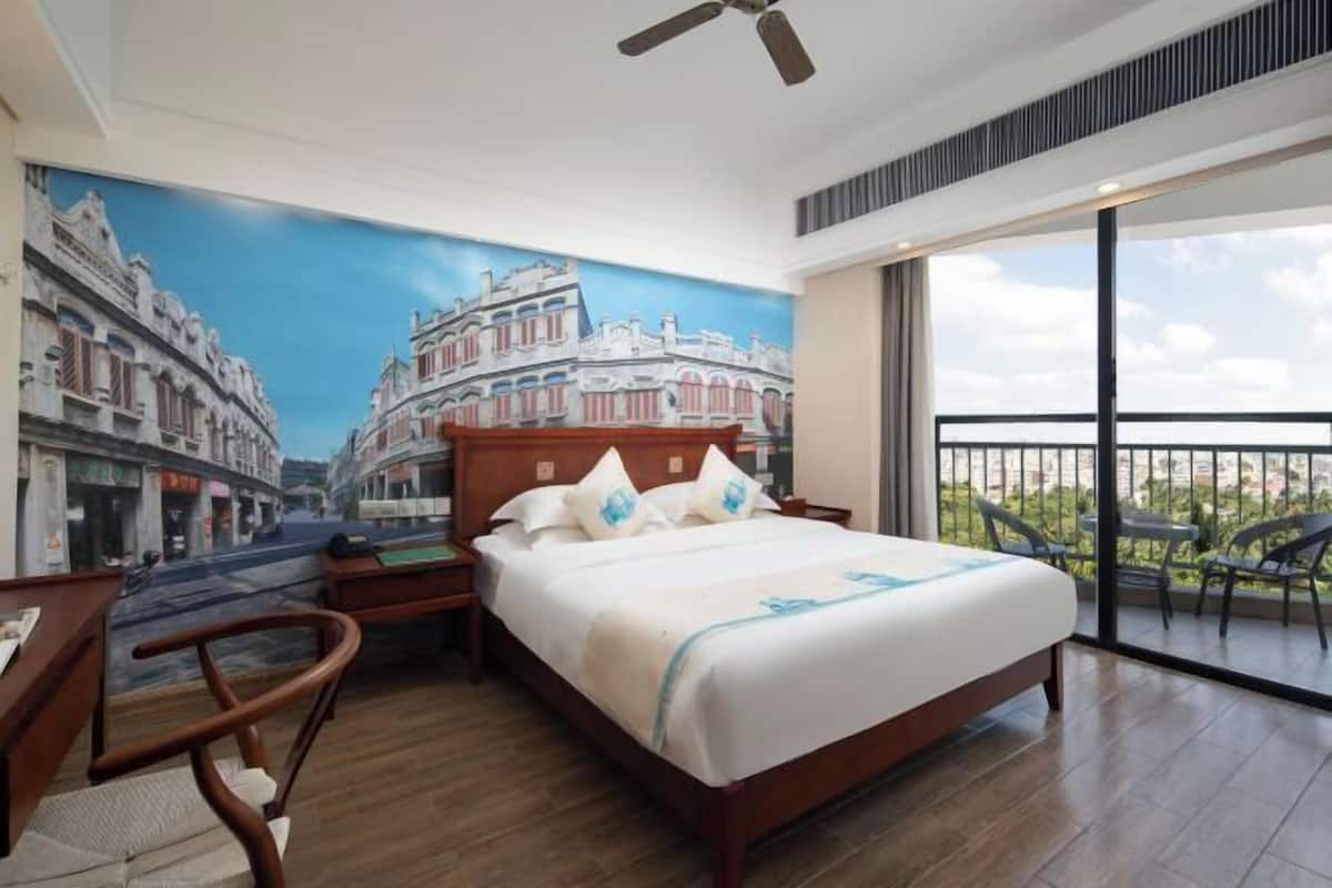 Une chambre d’hôtel comprenant un lit, un bureau, une chaise, un ventilateur de plafond, une grande fenêtre et un balcon.