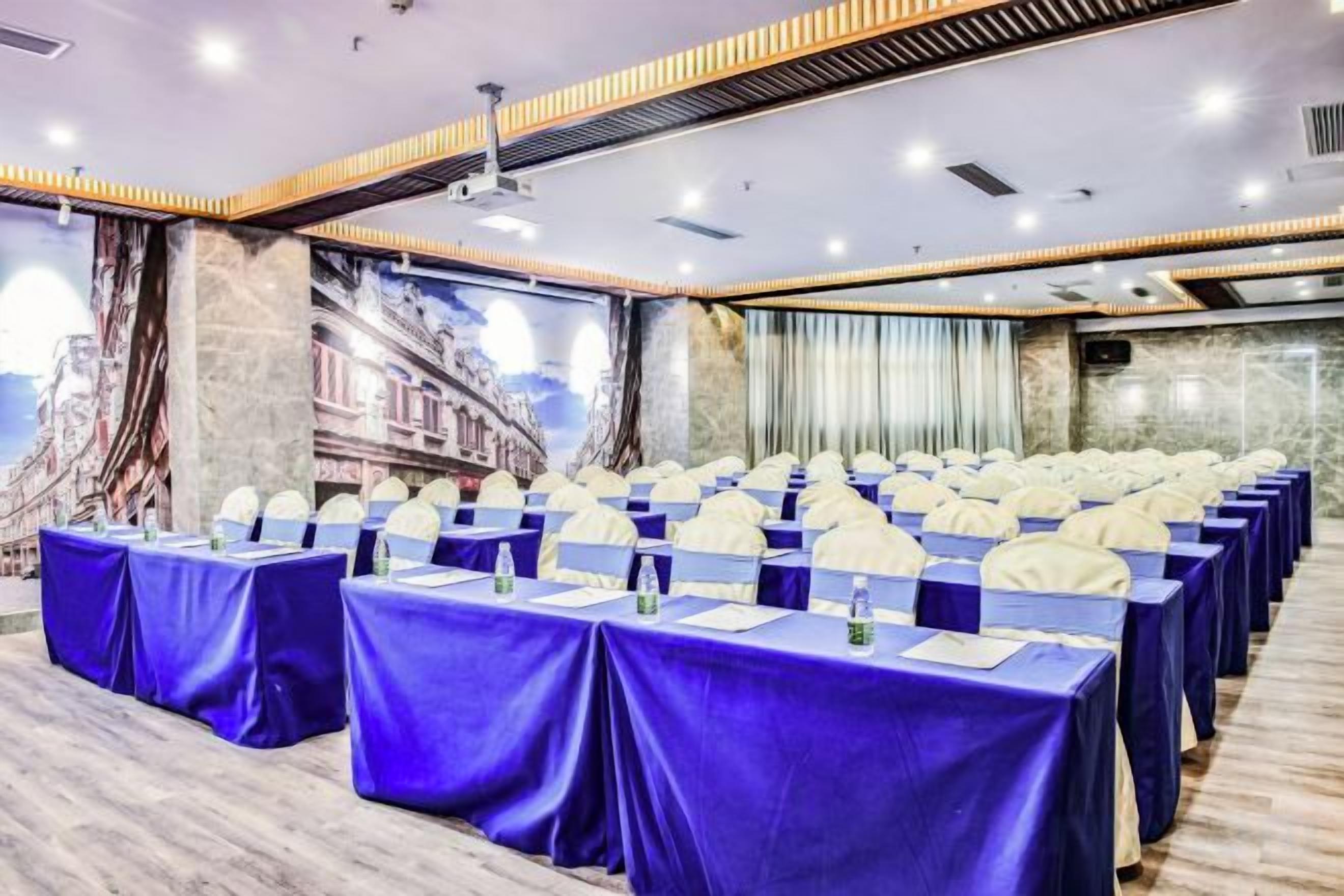 Uma sala de conferências com fileiras de mesas, cada uma com toalha azul e cadeiras brancas, preparada para uma reunião.