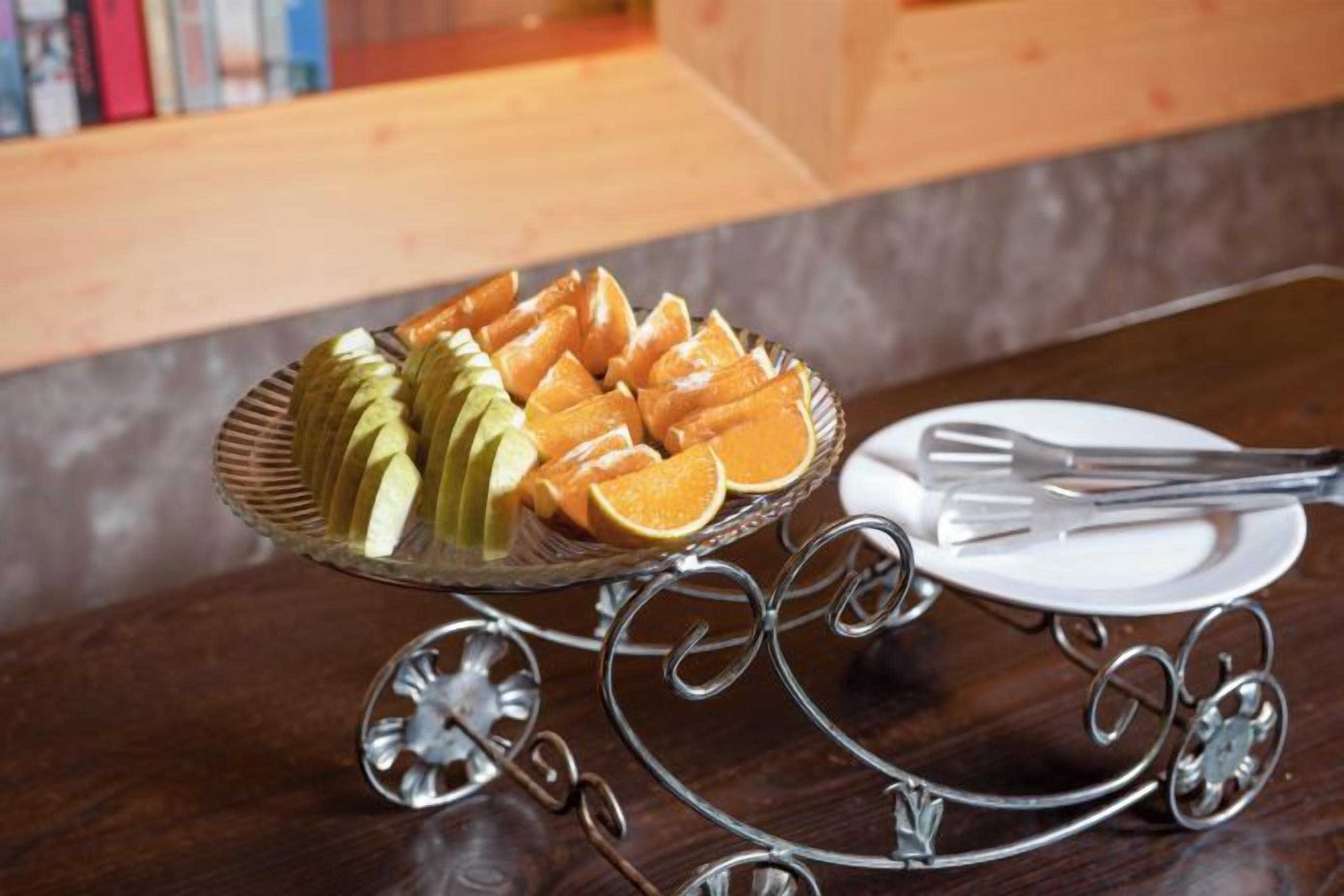 A fruit platter on a metal stand with a fork and a plate on a table.