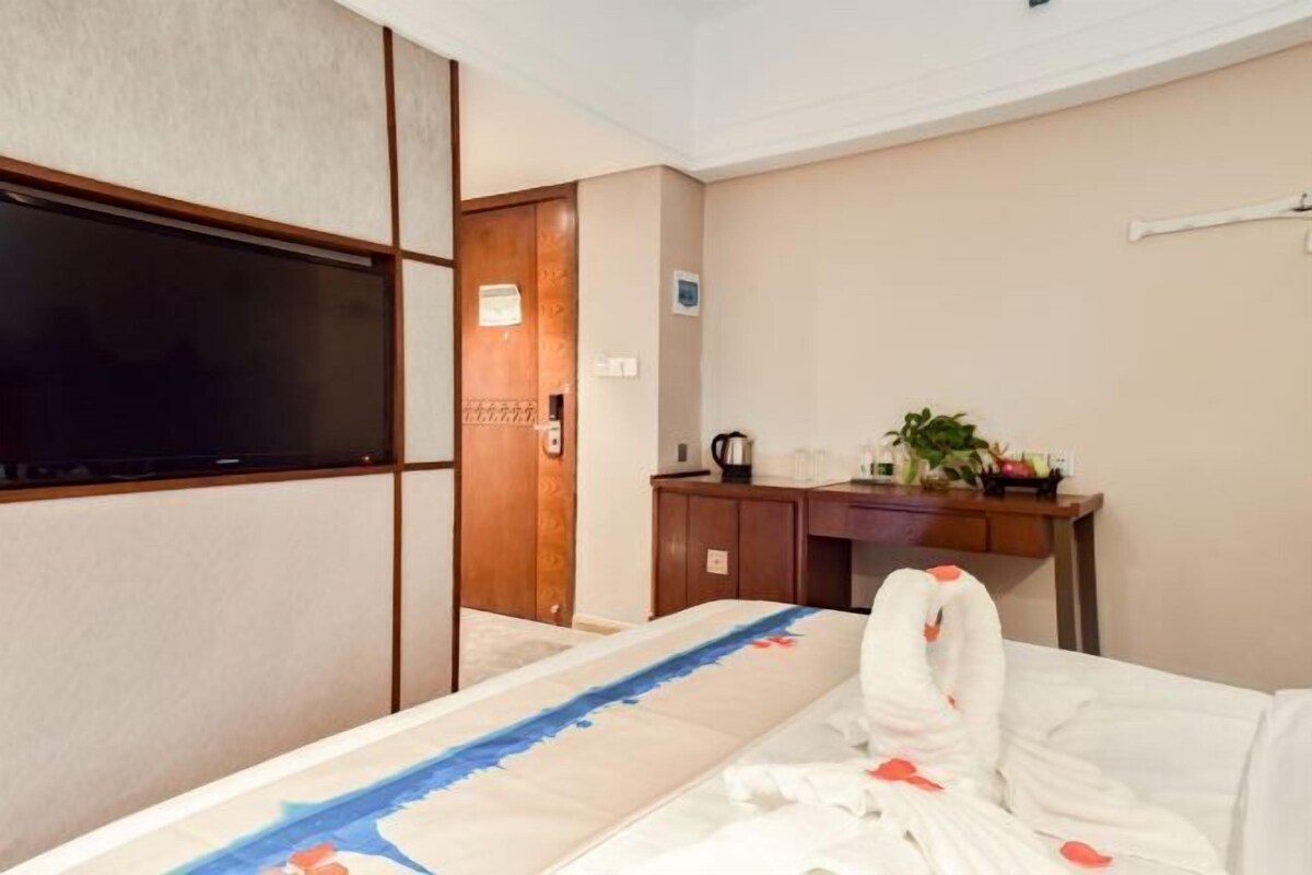 Une chambre d’hôtel avec un lit, un téléviseur fixé au mur, un bureau agrémenté d’une plante et une porte en bois.