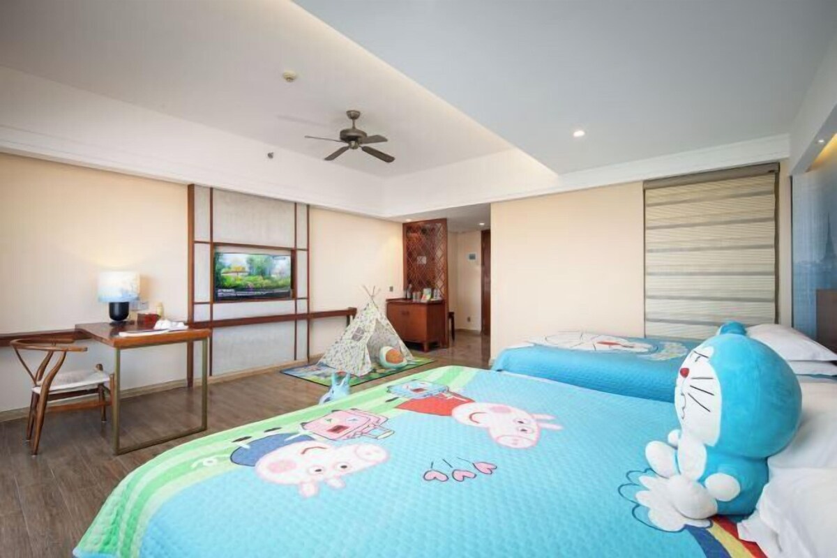 Une chambre d’hôtel avec deux lits, un bureau, une chaise, une télévision et un ventilateur de plafond.