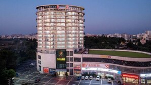 A multi-story hotel with a curved facade, multiple balconies, and a parking lot in front. - Wen Chang Tiancheng Hotel (Wenchang High-speed Railway Station Wennan Old Street Branch) (Wenchang)
