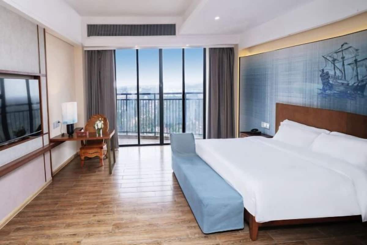 Une chambre d’hôtel avec un grand lit, un bureau avec une chaise, une télévision et un balcon avec vue.