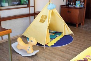 Une tente de jeu jaune avec une fenêtre, un cheval à bascule et un tapis coloré sur le sol.