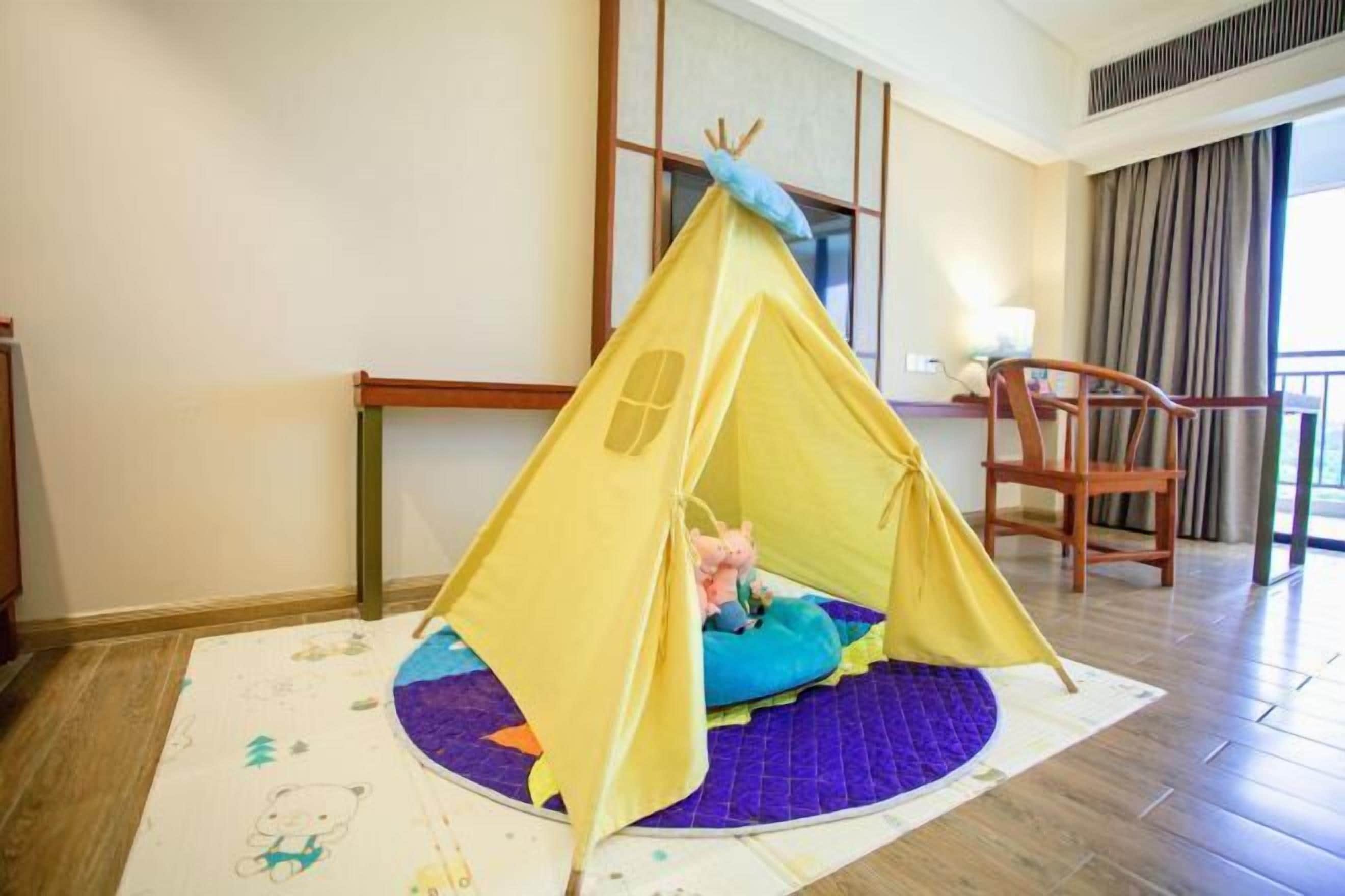 A room with a yellow tent-like structure on a purple mat, a wooden chair, and a window with curtains.