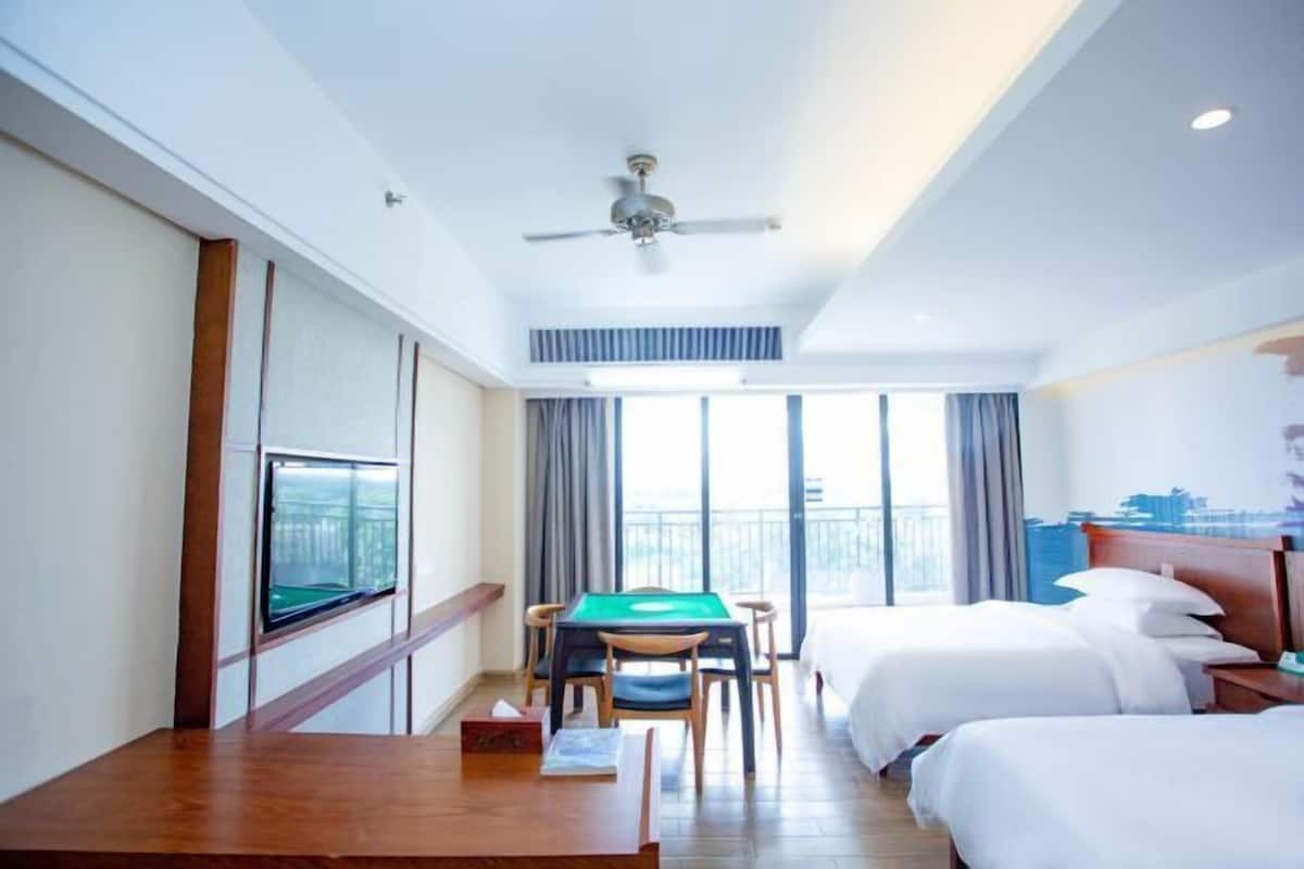 Une chambre d’hôtel avec deux lits, une télévision, une table avec des chaises et un balcon avec vue.