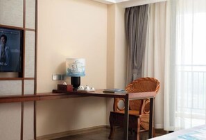 Une chambre d’hôtel avec un bureau en bois, une chaise en osier, une lampe et une affiche au mur.