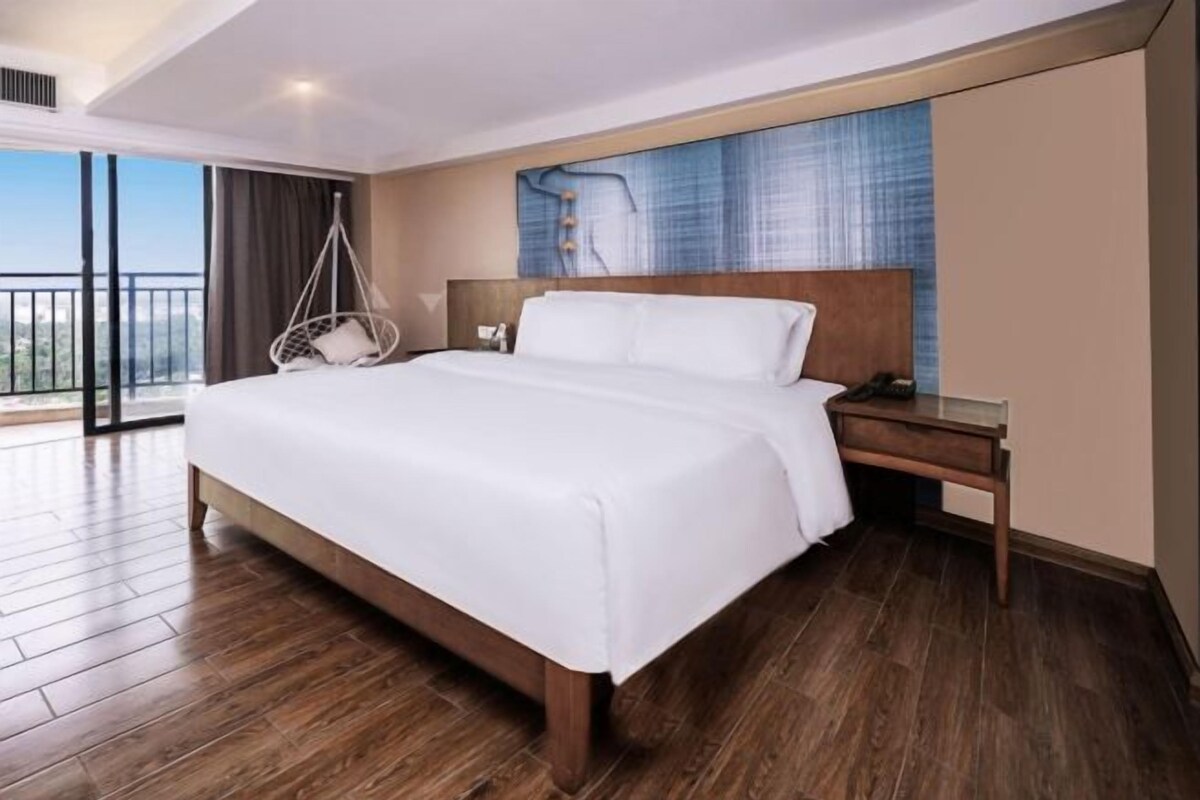 Una habitación de hotel con una cama grande, una mesita de noche de madera, un sillón colgante y vistas al exterior.