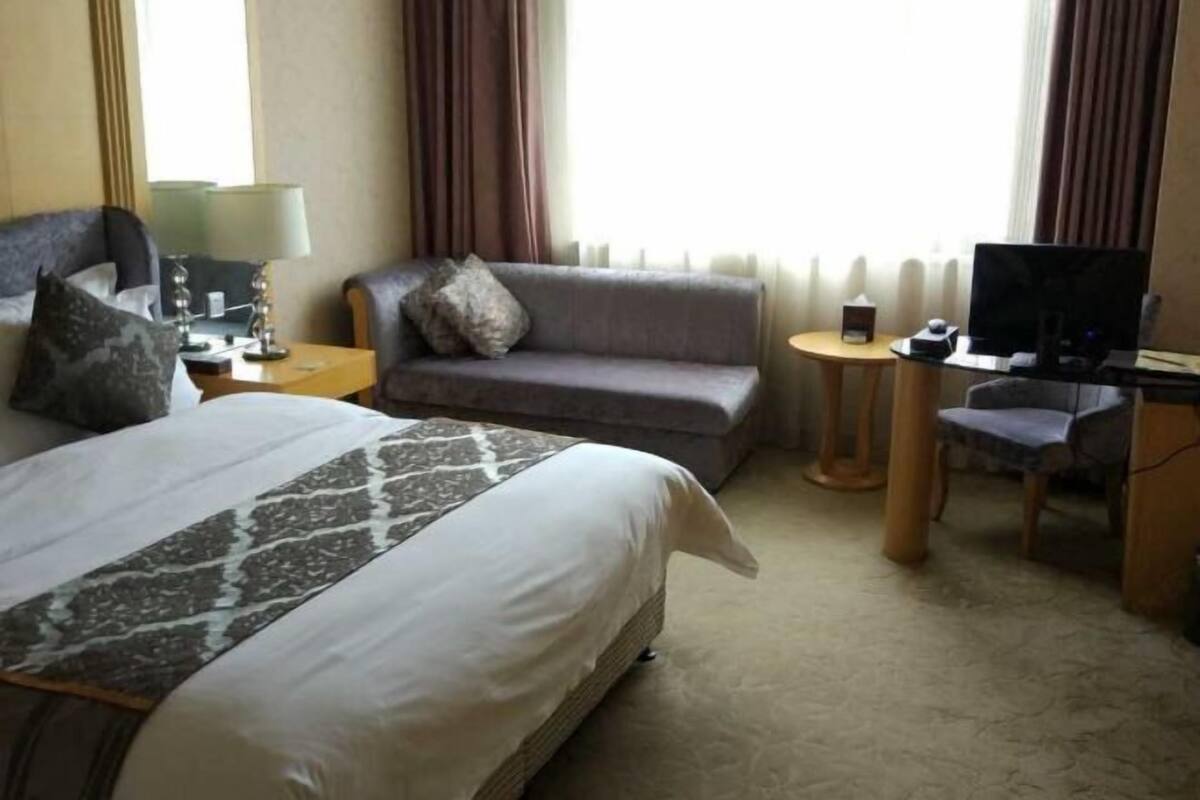 A hotel room with a bed, a sofa, a desk with a computer, and a chair.