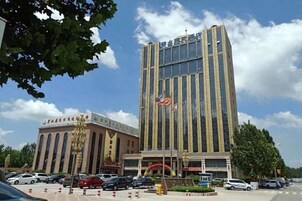 Un edificio de varios pisos con una destacada bandera estadounidense, rodeado de coches aparcados y árboles.