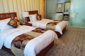A hotel room with two beds, a bedside table with a lamp, a mirror, a bathroom with a sink and mirror, and a patterned floor. - Bishui Lantian Hotel (Jing County)