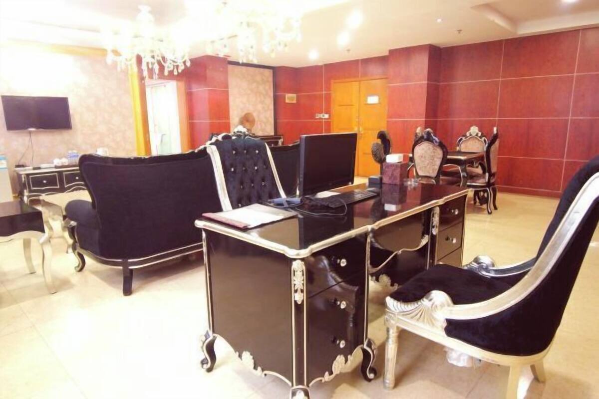 A conference room with a glass table, black and white upholstered chairs, a chandelier, and a television on the wall.