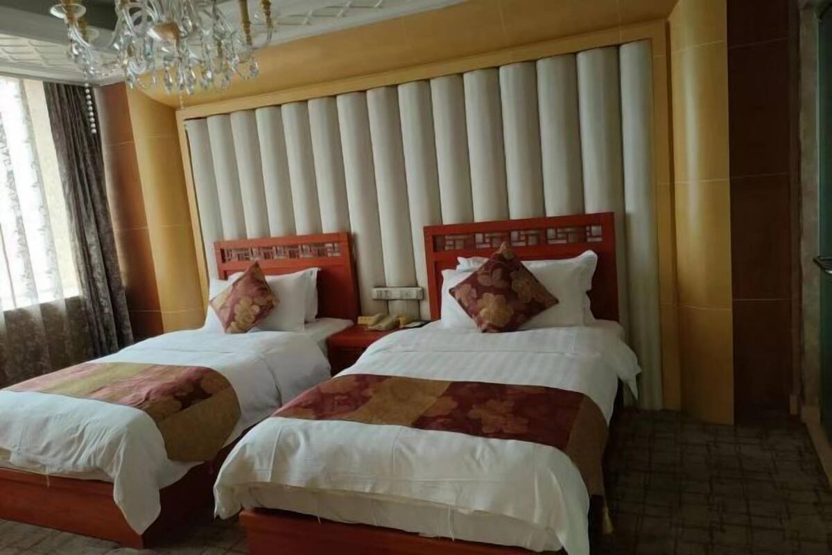 A hotel room with two beds, a chandelier, and a large window with curtains.