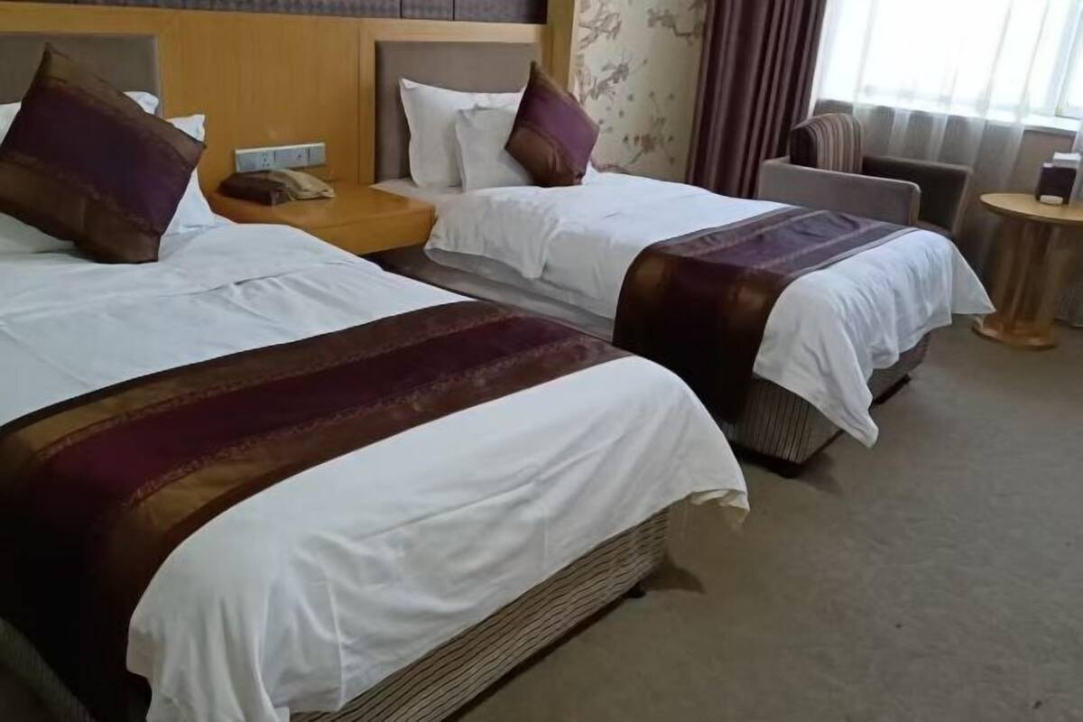 A hotel room with two beds, a nightstand, a chair, and a small table.