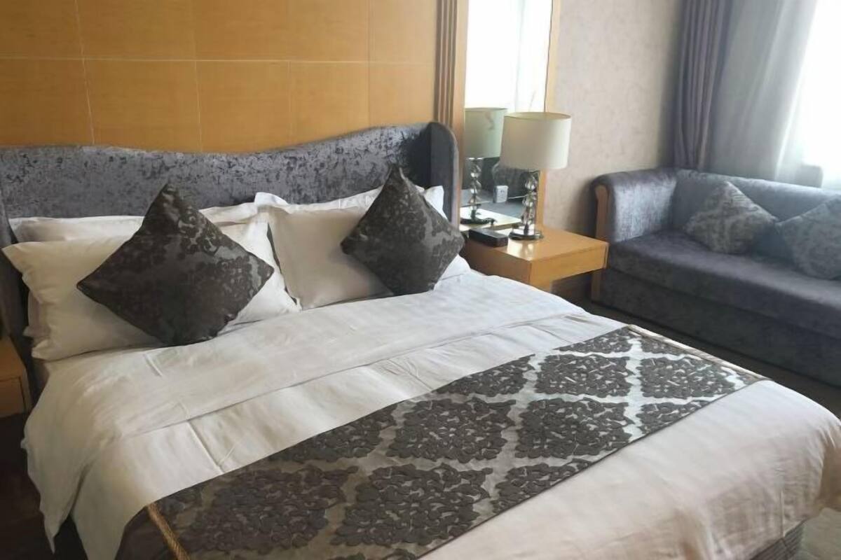 A hotel room with a bed, a nightstand, a lamp, and a sofa.