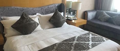 A hotel room with a bed, a nightstand, a lamp, and a sofa.