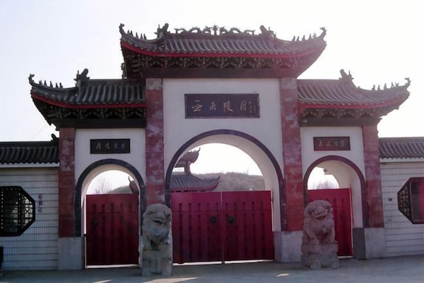 A traditional Chinese gate with two red doors and a central archway, flanked by stone lion statues.