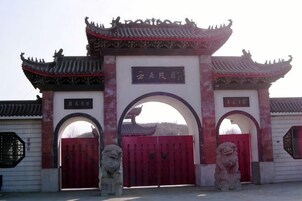 A traditional Chinese gate with two red doors and a central archway, flanked by stone lion statues.