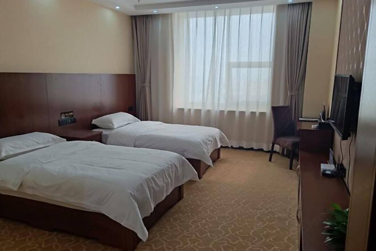 A hotel room with two beds, a desk, a chair, a TV, and a window with curtains.