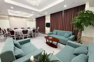 Habitación de hotel con zona de comedor, un conjunto de sofás, una mesa de centro y una planta grande.