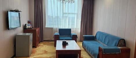 A hotel room with a sofa, two armchairs, a coffee table, a TV, and a small refrigerator.