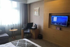 A hotel room with a bed, a desk with a computer, a chair, a small table, a TV mounted on the wall, and a window with curtains. - Bishui Lantian Hotel (Jing County)