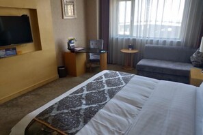 A hotel room with a bed, a desk, a chair, a sofa, a TV, and a window with curtains. - Bishui Lantian Hotel (Jing County)