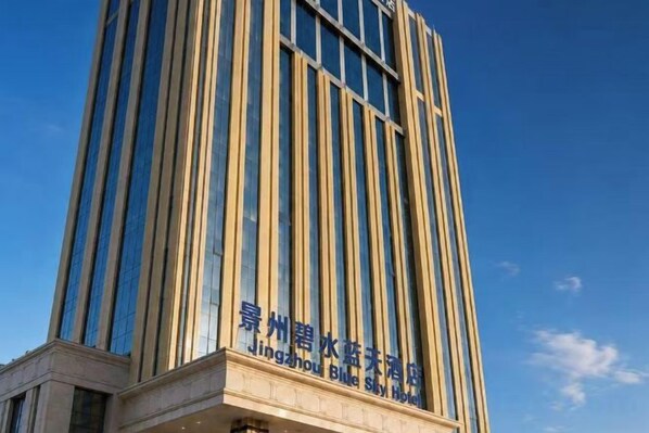Un edificio alto con líneas verticales y un letrero que indica que es el Hotel Jingzhou Blue Star.