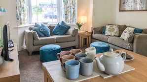A cozy living room with two sofas, a coffee table with mugs and a teapot, and a window with curtains. - I just love the location of Arthur’s Place within ’The Bay’. (Filey)