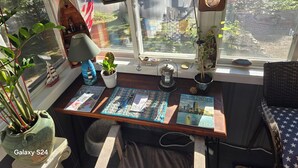 A cozy reading nook with a window view, a lamp, a small sailboat model, and a book titled "Boston Common". - Cozy Lakeside Cottage Just Steps To The Beach (Mashpee)