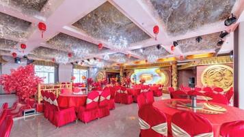 A banquet hall with round tables and chairs, a stage with a large screen, and red decorations.