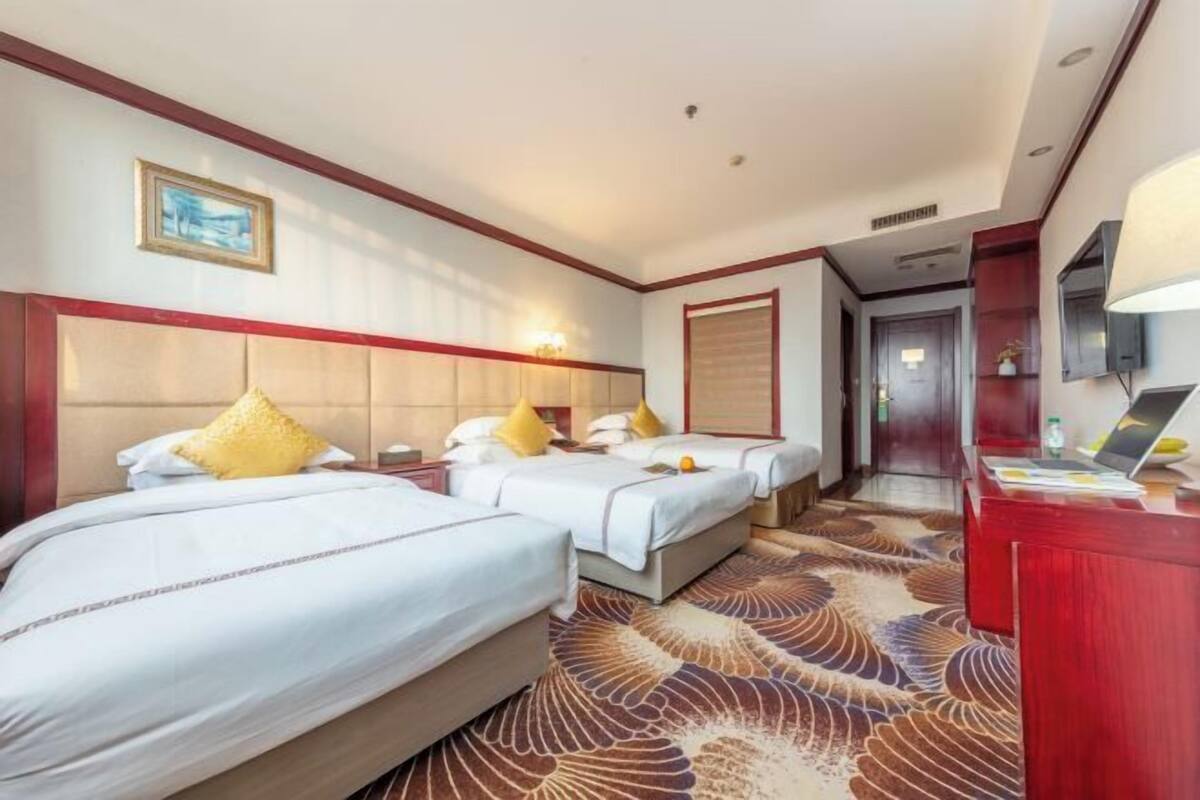 Une chambre d’hôtel avec trois lits, un bureau et une télévision.