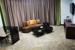 Una sala de estar con un sofá de cuero marrón, una mesa de centro negra, un televisor sobre un mueble bajo y una alfombra estampada.