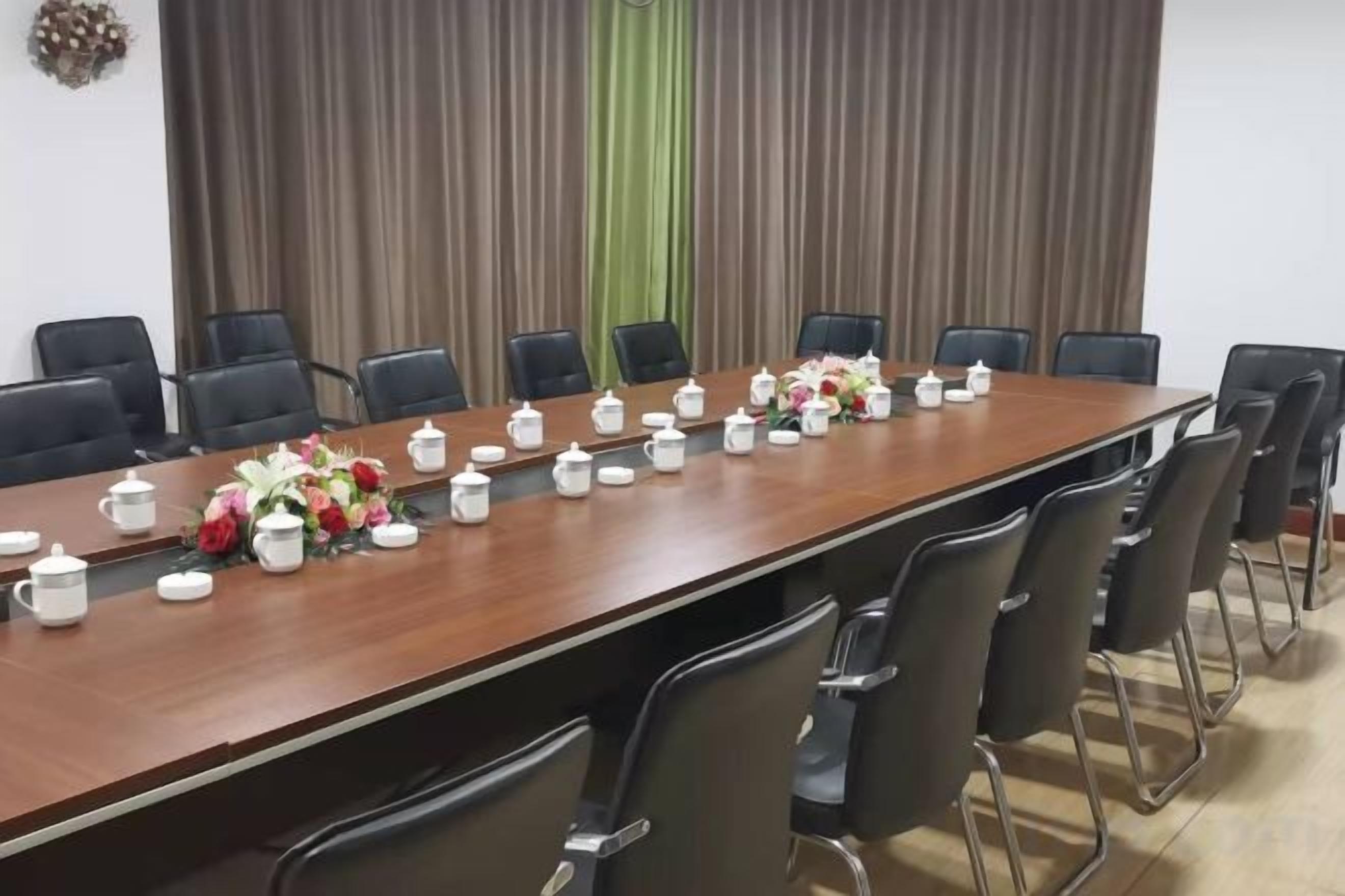 Une salle de conférence avec une longue table, des chaises et des centres de table ornés de fleurs.