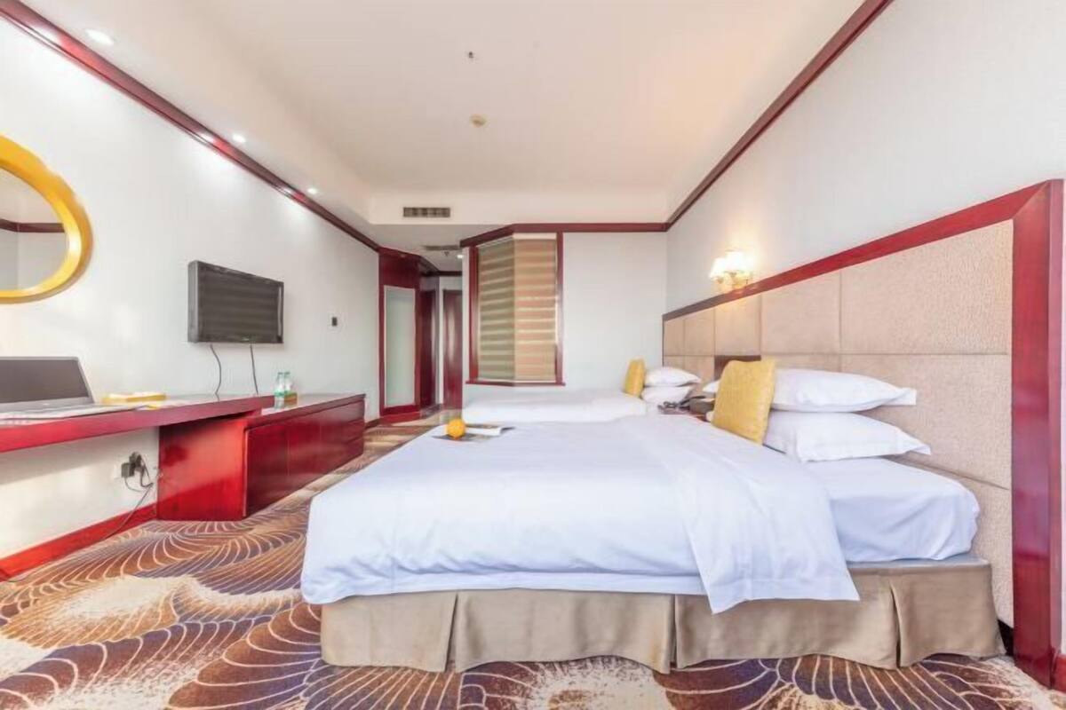 Une chambre d’hôtel avec un grand lit, un bureau avec un ordinateur portable, une télévision et un miroir.