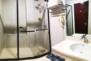 Une salle de bain avec une douche à parois de verre, un lavabo blanc et une porte en bois foncé.
