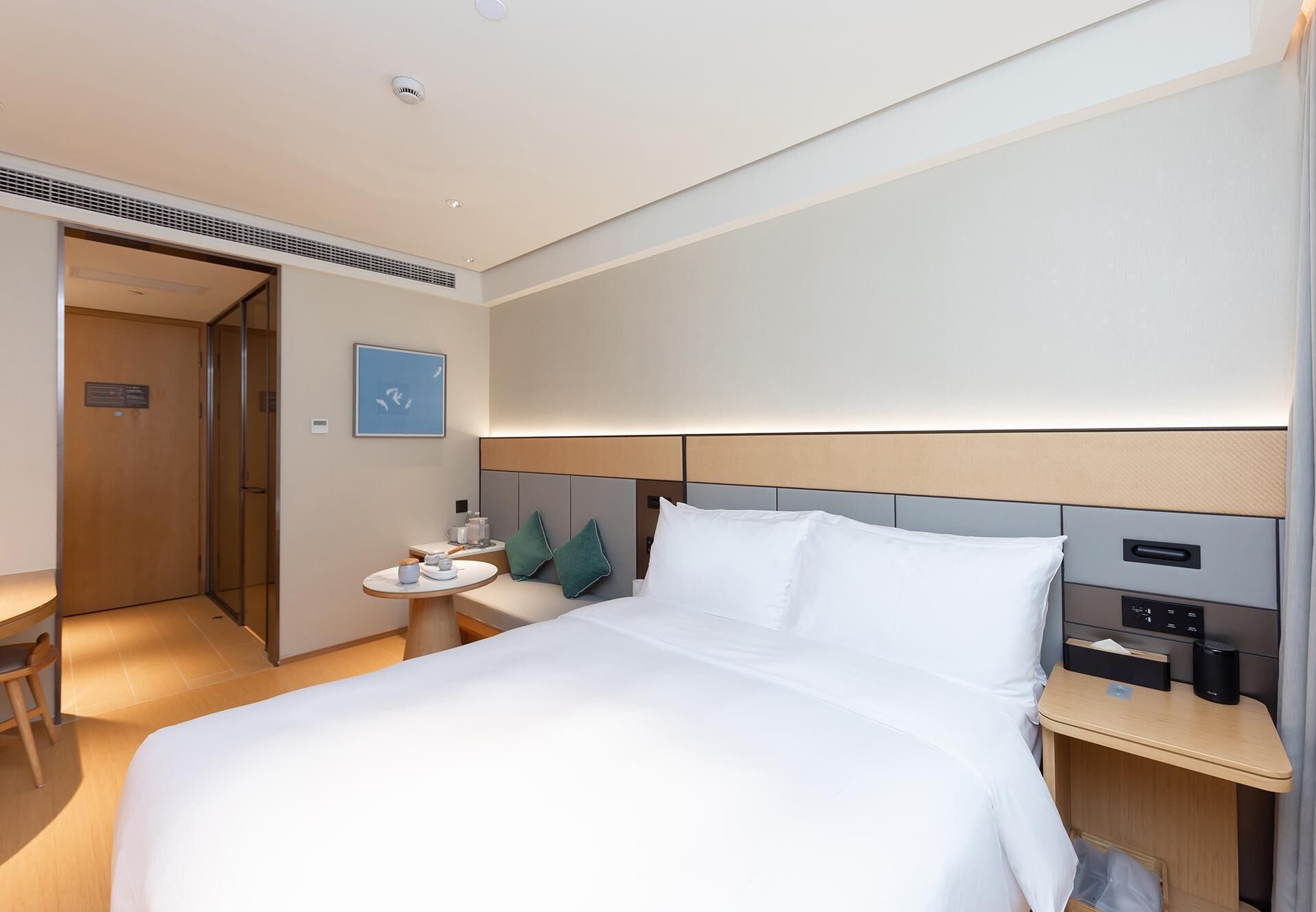 Habitación de hotel con cama, mesitas de noche, escritorio, silla, puerta y lámpara en la pared.