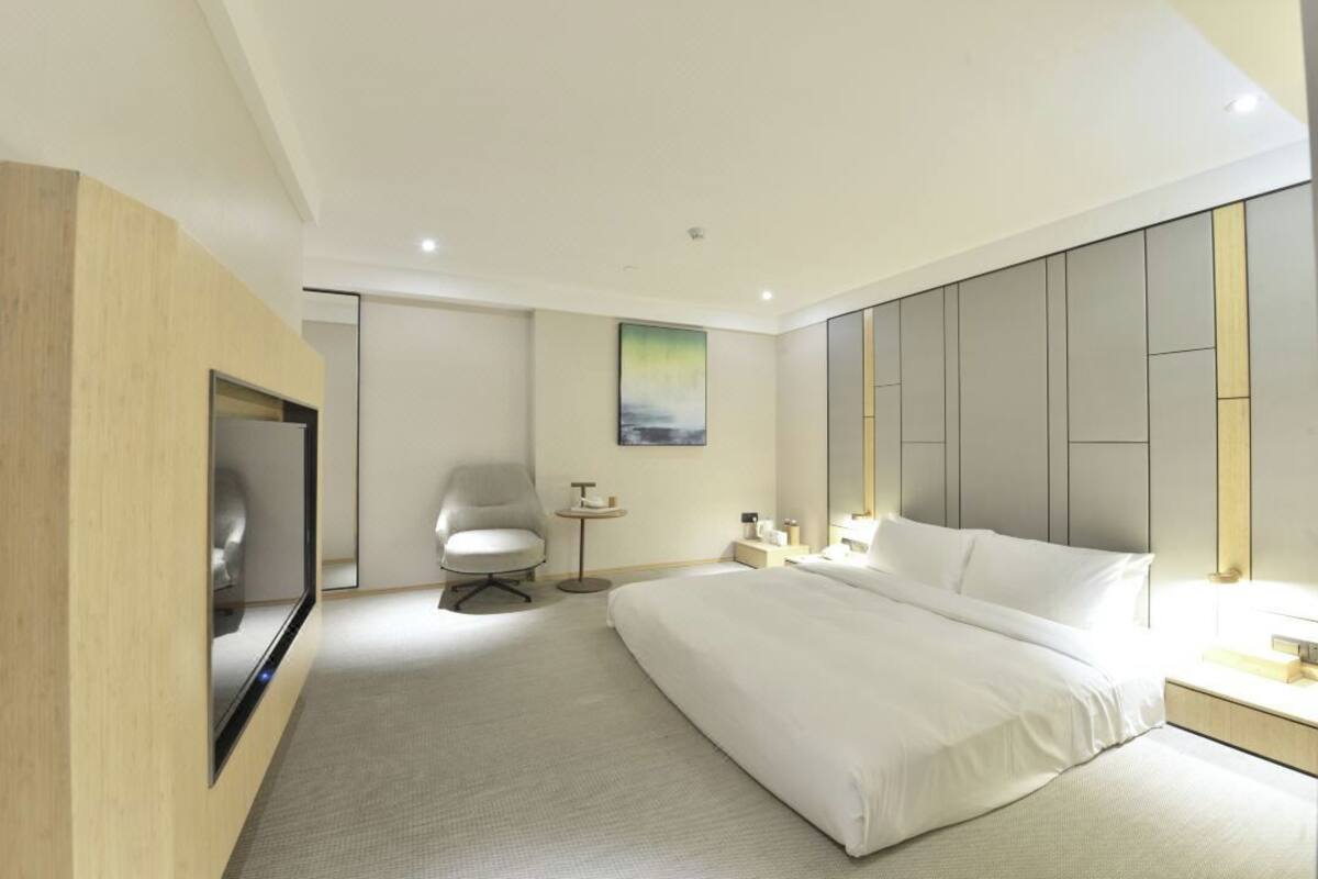 A modern hotel room with a large bed, a TV, a chair, a small table, and a painting on the wall.