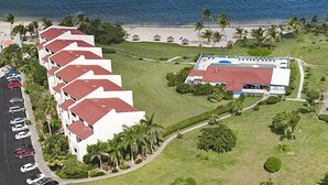 A hotel with multiple white buildings with red roofs, a large pool, and a beach area with palm trees.