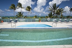 Piscina com borda azul, cercada por palmeiras e céu claro.