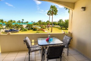 A balcony with a table and chairs, overlooking a parking area and a view of palm trees and a beach. - Comfy condo minutes from downtown & Free Parking (Christiansted)