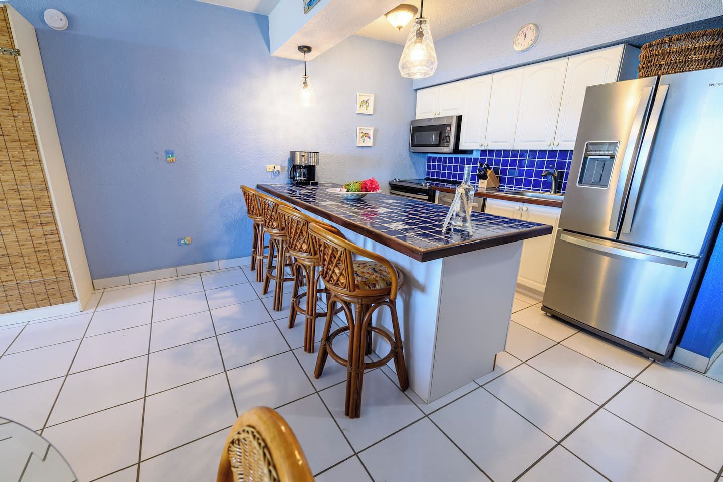 Una cocina con una isla central, taburetes de bar, un refrigerador y un microondas.