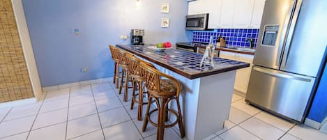Una cocina con una isla central, taburetes de bar, un refrigerador y un microondas.