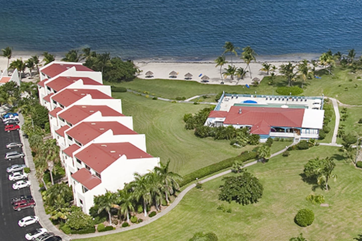 A hotel with multiple white buildings, a large pool area, and a beachfront.