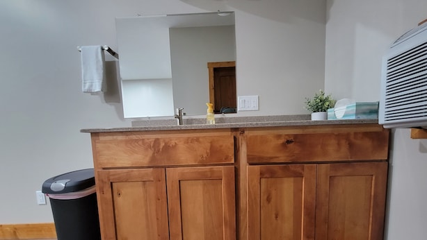 Una cocina con armarios de madera, una encimera, un cubo de basura, un lavabo y un espejo.