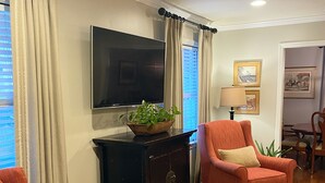 Een woonkamer met een televisie, twee fauteuils, een donker houten kast en een kamerbreed tapijt met dessin.